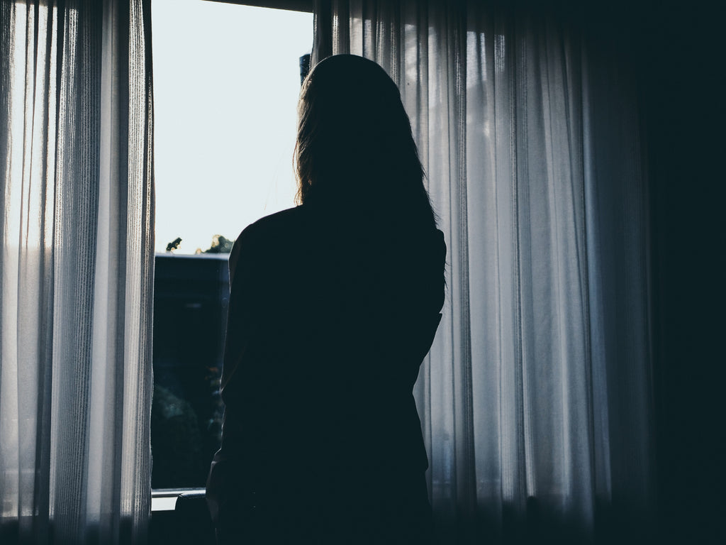 woman standing in dark room near window and ways to make your room dark for better sleep