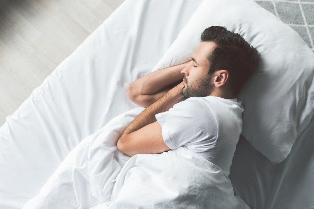 Young man asleep on a white bed and mattress