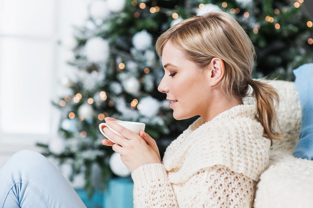 Young woman drinking tea and relaxing by the Christmas tree