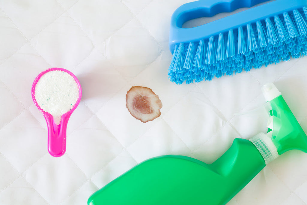 Stain on white mattress. Green spray bottle, pink cup or scoop of washing powder and blue brush.